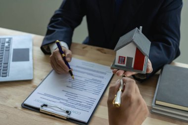 Emlakçılar kontratta konut satın alma ya da kiralama teklifinde bulunup açıklar. İşadamları küçük bina tasarımlarını ve emlak sigortasını ofisteki masada tutarlar..