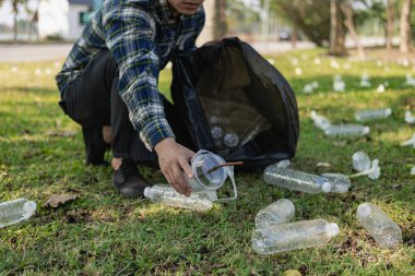 Adamın elleri çöp topluyor, boş plastik su şişeleri, yerde yahni, kuru yapraklar, çöp torbalarında plastik şişeler, temizlik, toprak ekoloji günü konsepti...