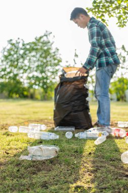 Adamın elleri çöp topluyor, boş plastik su şişeleri, yerde yahni, kuru yapraklar, çöp torbalarında plastik şişeler, temizlik, toprak ekoloji günü konsepti...