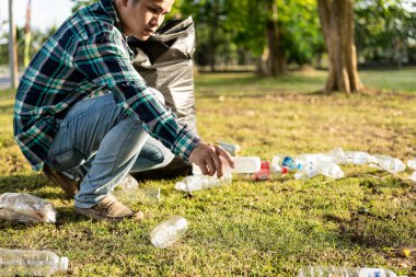 Adamın elleri çöp topluyor, boş plastik su şişeleri, yerde yahni, kuru yapraklar, çöp torbalarında plastik şişeler, temizlik, toprak ekoloji günü konsepti...