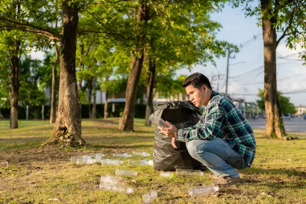 Adamın elleri çöp topluyor, boş plastik su şişeleri, yerde yahni, kuru yapraklar, çöp torbalarında plastik şişeler, temizlik, toprak ekoloji günü konsepti...
