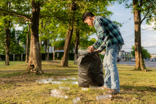 Adamın elleri çöp topluyor, boş plastik su şişeleri, yerde yahni, kuru yapraklar, çöp torbalarında plastik şişeler, temizlik, toprak ekoloji günü konsepti...