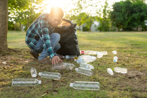 Adamın elleri çöp topluyor, boş plastik su şişeleri, yerde yahni, kuru yapraklar, çöp torbalarında plastik şişeler, temizlik, toprak ekoloji günü konsepti...