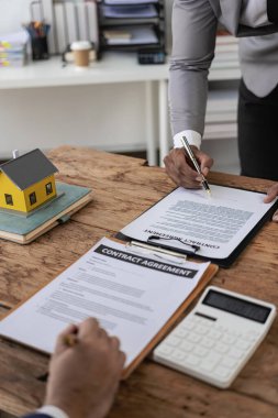 Emlakçı ev satın alma sözleşmesinin şartlarını tartışır ve müşteriden sözleşmeye yasal olarak girmek için belgeyi imzalamasını ister. dikey resim