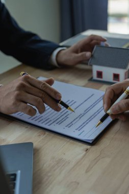 Emlakçı ev satın alma sözleşmesinin şartlarını tartışır ve müşteriden sözleşmeye yasal olarak girmek için belgeyi imzalamasını ister. dikey resim