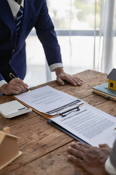 The real estate agent discusses the terms of the home purchase contract and asks the client to sign the document to legally enter into the contract. vertical image