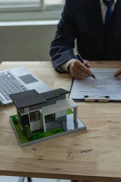 The real estate agent discusses the terms of the home purchase contract and asks the client to sign the document to legally enter into the contract. vertical image