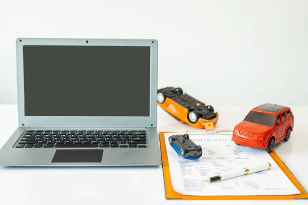 Laptop computer and car model with insurance contract documents on table, insurance concept