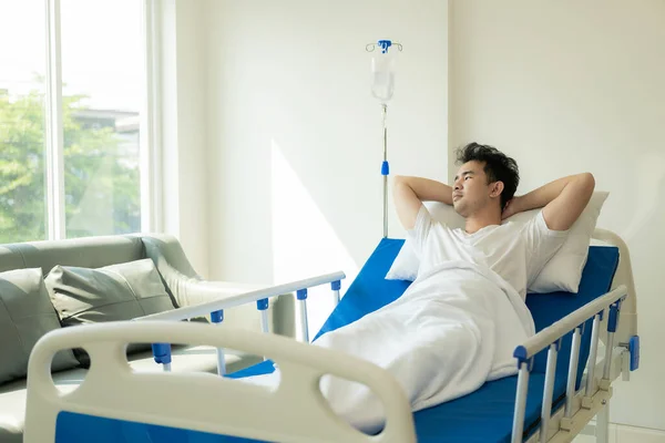 Young Asian man, patient lying on hospital bed, undergoing treatment in medical clinic. Health insurance or hospitality concept