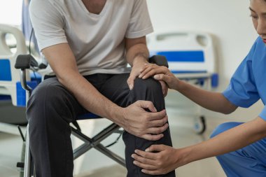 Genç Asyalı bir adam fizyoterapist gözetiminde kadın bir fizyoterapistle jimnastik yapıyor. Omurga ve bacaklardaki ağrıyı tedavi eder.