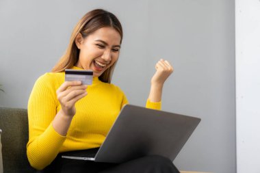 Asyalı bir kız, bilgisayarını kullanarak akıllı telefon ve kredi kartını cep telefonu ya da internet üzerinden alışveriş uygulaması kullanarak evden alışveriş yapıyor..