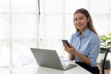 Akıllı telefondan çalışan Asyalı iş kadını akıllı telefonla konuşuyor ve ofiste çalışıyor. Asyalı iş kadını muhasebeci, ofiste duran veri belgesi.