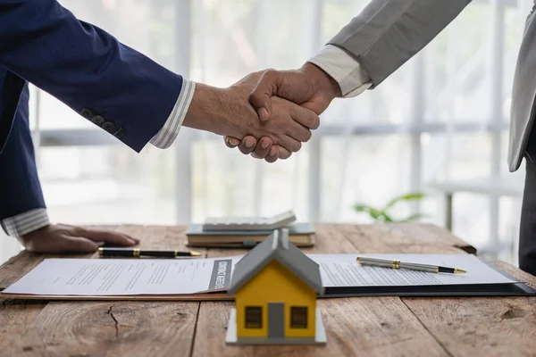 Hands holding hands signing a contract for buying a house or renting a house on a desk Real estate agent and client shaking hands after signing a real estate purchase contract,