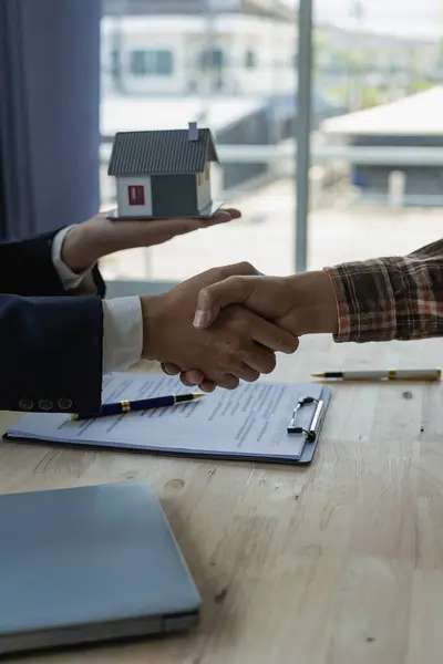 Hands holding hands signing a contract for buying a house or renting a house on a desk Real estate agent and client shaking hands after signing a real estate purchase contract,