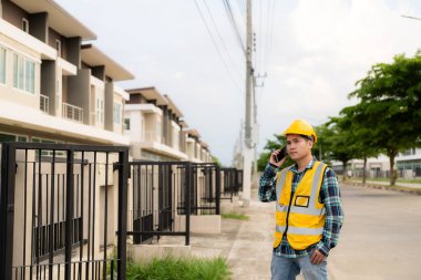 Genç Asyalı mühendis inşaat alanında sarı bir şapka takarak ve iş yerinde bir yapı inşa etmekle ilgili çalışmalarını teftiş ediyor..
