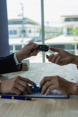 Araba kiralama işindeki müşterilerin elinde araba anahtarlarını tutan genç satıcı Asyalı erkek satış temsilcisi müşterilere önemli arabalar satıyor..