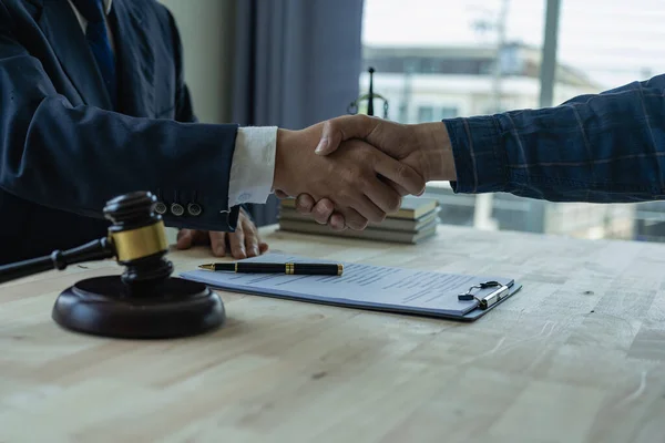 A lawyer shakes hands with a client who is making documents, contracts, agreements, cooperation agreements with clients at the lawyer\'s desk in a law office. and the hammer of justice on the table.