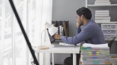 Finansal analist, masaüstü bilgisayarının önünde oturan genç erkek işçinin elektronik satış istatistikleri kağıdını incelediğini görüyor