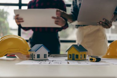 Mimar, tasarım mühendisi, tasarım planlama üzerinde çalışan inşaat mühendislerinden oluşan bir grup bina planına bakıyor ve dizüstü bilgisayarla bina tasarımı projesinin yakın plan resimlerini çiziyor.