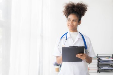 Klinikte çalışan, bilgisayarla klinikte çalışan, laptopa bakan, hastalarla video konferansı yapan, online danışmanlık konsepti olan Afro-Amerikalı genç bir kadın..