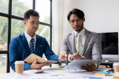Şirket mali istatistiklerini, beyin fırtınası fikirlerini ve masadaki grafik dokümanlarını incelemek için birlikte çalışan iki iş adamı..