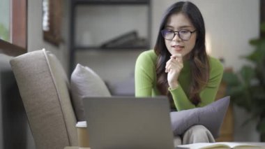 Çekici Asyalı kadın çalışıyor, internette sörf yapıyor, dizüstü bilgisayar kullanıyor, evden oturma odasına geçip neşeli bir ifadeyle çalışıyor..