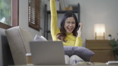 Sosyal medya için akıllı telefon kullanan gülümseyen Asyalı kadın, evde oyunlar oynayan, mutlu hisseden, evde mesajlaşan ve alışveriş yapan. Evdeki yaşam tarzı kadını