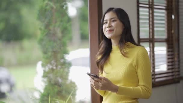 スマートフォンを使った笑顔のアジア人女性は ソーシャルメディアでゲームをしたり 自宅で幸せを感じたり テキストを送ったり 自宅でショッピングしたりしています 自宅でのライフスタイル女性 — ストック動画