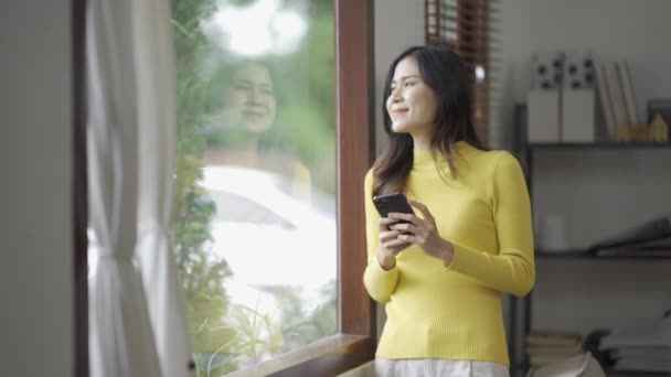 スマートフォンを使った笑顔のアジア人女性は ソーシャルメディアでゲームをしたり 自宅で幸せを感じたり テキストを送ったり 自宅でショッピングしたりしています 自宅でのライフスタイル女性 — ストック動画