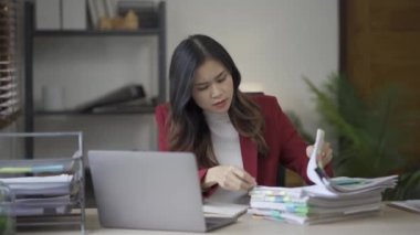 Takım elbiseli stresli Asyalı iş kadını ofis evraklarını doldurma konusunda endişeli. Masadaki belgelerle hayal kırıklığına uğramış bir kadın.