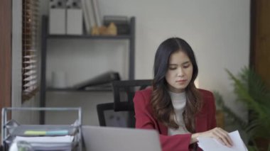 Takım elbiseli stresli Asyalı iş kadını ofis evraklarını doldurma konusunda endişeli. Masadaki belgelerle hayal kırıklığına uğramış bir kadın.