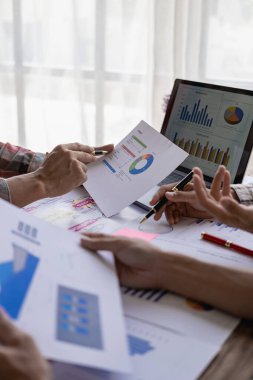 Şirket toplantısı sırasında dizüstü bilgisayar ve dizüstü bilgisayardaki mali raporların analizi başarılı bir takım çalışmasının dikey yakın plan resmini gösteriyor.