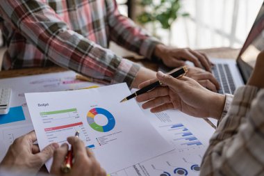 Genç iş adamlarının iş stratejilerini analiz etmek ve planlamak için dizüstü bilgisayar ve finansal rapor belgeleriyle beyin fırtınaları. Resmi kapat.