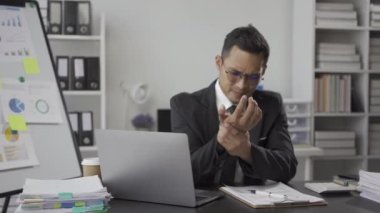 Asyalı iş adamı acıdan kurtulur, işten yorulur, uyur ve uzun süre masa başında oturmaktan sıkılır ve ofis sendromlu adam dinlenmek ve ofiste mola vermek için kollarını uzatır..