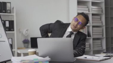 Asyalı iş adamı acıdan kurtulur, işten yorulur, uyur ve uzun süre masa başında oturmaktan sıkılır ve ofis sendromlu adam dinlenmek ve ofiste mola vermek için kollarını uzatır..