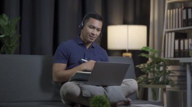 Genç siyah saçlı bir adam kanepeye oturur ve dizüstü bilgisayarıyla çalışır. Uzaktan çalışan genç adam kulaklık takıyor, film izliyor, sıradan bir günde evde müzik dinliyor..