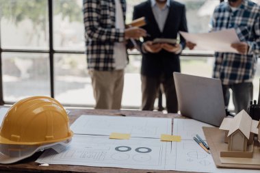 Üç inşaat işçisi oturup inşaat planlarını tartışıyor. Ustabaşı ve mühendislerden oluşan bir ekip, işe başlamadan önce evin planlarını kontrol etmek için inşaat alanının planlarıyla konuşuyorlar..