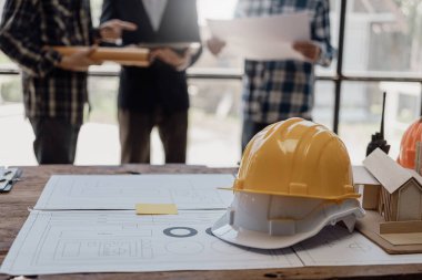 Üç inşaat işçisi oturup inşaat planlarını tartışıyor. Ustabaşı ve mühendislerden oluşan bir ekip, işe başlamadan önce evin planlarını kontrol etmek için inşaat alanının planlarıyla konuşuyorlar..