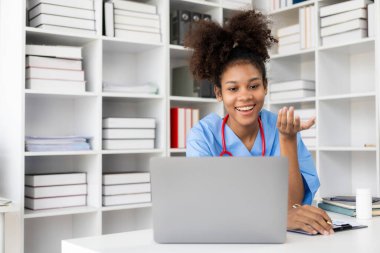 Beyaz önlüklü ve steteskoplu başarılı Amerikalı kadın doktor hastanede dizüstü bilgisayarla çalışıyor, hastalara danışmanlık yapıyor..