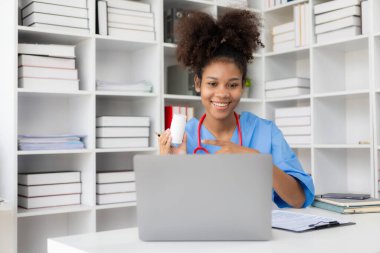 Beyaz önlüklü ve steteskoplu başarılı Amerikalı kadın doktor hastanede dizüstü bilgisayarla çalışıyor, hastalara danışmanlık yapıyor..