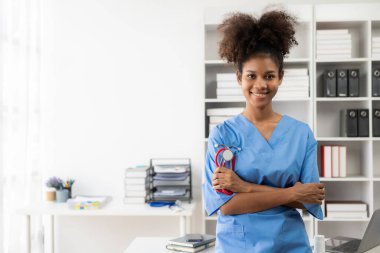 Beyaz önlüklü ve steteskoplu başarılı Amerikalı kadın doktor hastanede dizüstü bilgisayarla çalışıyor, hastalara danışmanlık yapıyor..
