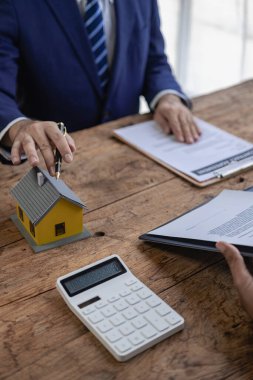 Bir emlakçı ev satın alma sözleşmesinin şartlarını tartışır ve müşteriden yasal olarak sözleşme imzalaması için belgeleri imzalamasını ister. Bir ev satıyorum. Yakın plan fotoğraf..