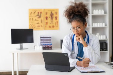 Kendine güvenen Afrikalı kadın doktor uzak online danışmanlık sağlamak için ofiste tablet kullanıyor ya da bir internet sohbetinde iş arkadaşlarıyla buluşuyor..