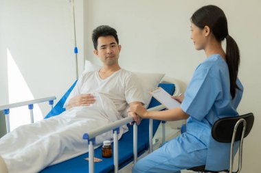 Asyalı kadın doktor, sağlık kontrolü için hastanın yatağında yatan bir erkeğe bakıcılık ve danışmanlık yapıyor. Tıbbi konsept. Sağlık kontrolü. Asya modeli.