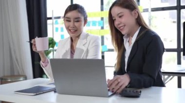 Dizüstü bilgisayarda çalışan iki Asyalı iş kadını, pazarlama projesi belge analizinde mali verileri tartışıyor. 4k