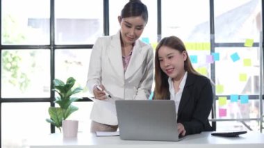 Dizüstü bilgisayarda çalışan iki Asyalı iş kadını, pazarlama projesi belge analizinde mali verileri tartışıyor. 4k