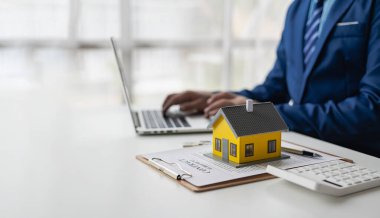Emlakçı ya da borsacı belgelerle, ev ipoteği sözleşmeleriyle, kredi fikirleriyle ve kendi mallarıyla çalışır. Küçük bir model eve yakın çekim