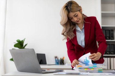 Genç Asyalı kadın iş yerinde dizüstü bilgisayar ve finansal belgeler kullanarak çalışıyor, serbest çalışan, online pazarlama, tele pazarlama, e-ticaret