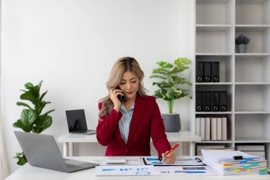 Genç Asyalı kadın iş yerinde dizüstü bilgisayar ve finansal belgeler kullanarak çalışıyor, serbest çalışan, online pazarlama, tele pazarlama, e-ticaret