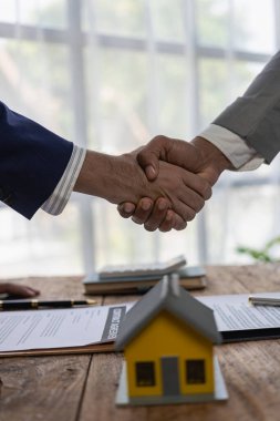 Emlakçılar ofiste el sıkışıyor müşteri, sözleşmeyi imzalamak için simsar ve satıcıyla görüşüyor. Bir satış temsilcisi bir müşteriye ev ya da daire satın almak için ev satın alma sözleşmesi önerir. Yakın plan resimler.